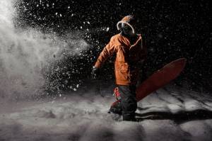 Профессиональный сноубордист в оранжевой спортивной одежде с доской ночью
